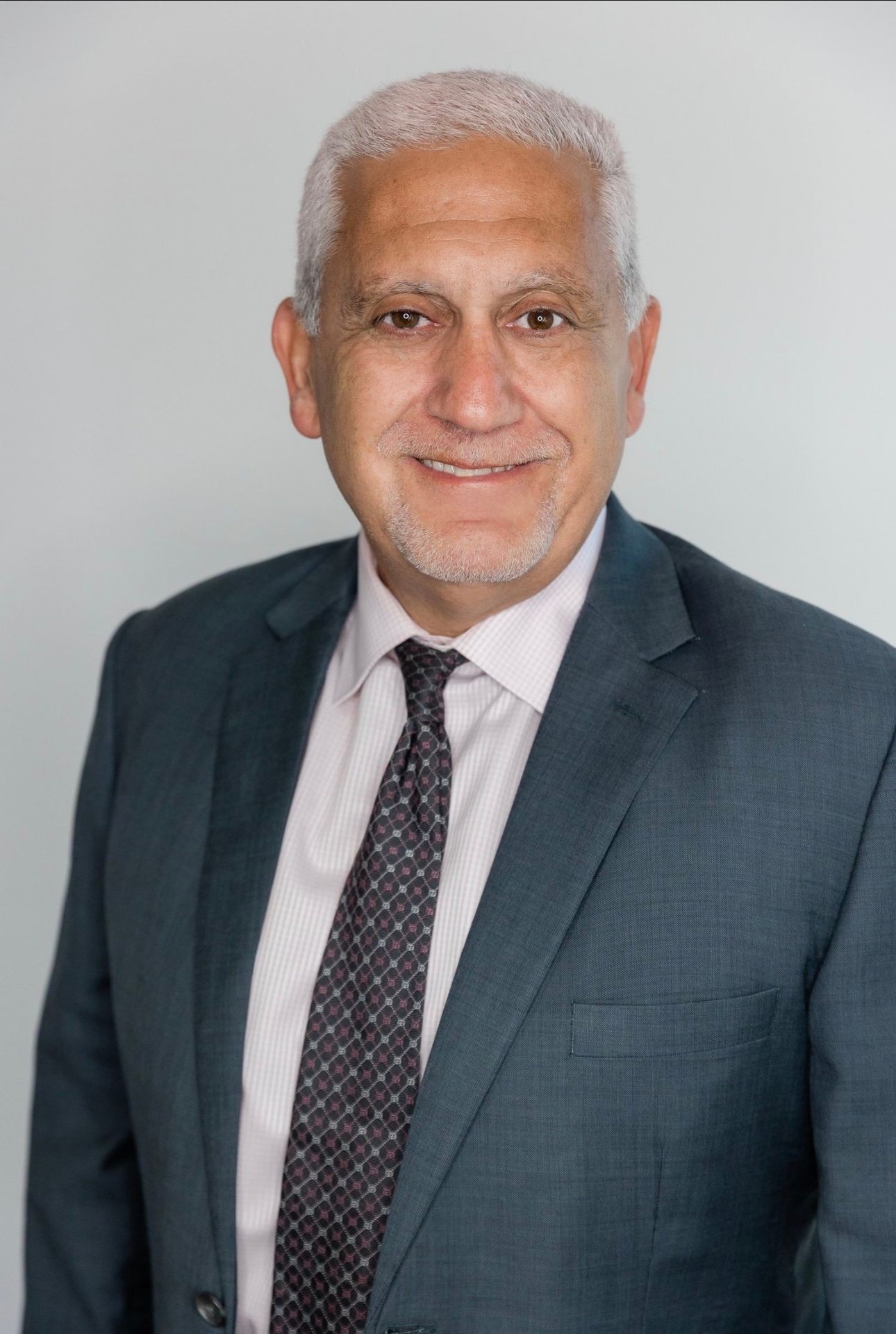 Smiling man in a suit and tie against a gray background.