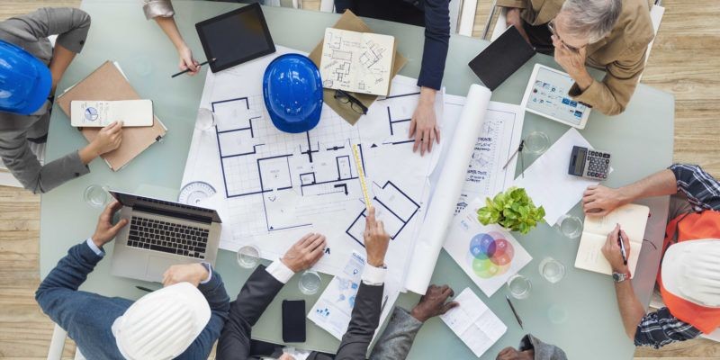 Team wearing helmets and reviewing architectural blueprints on a table.